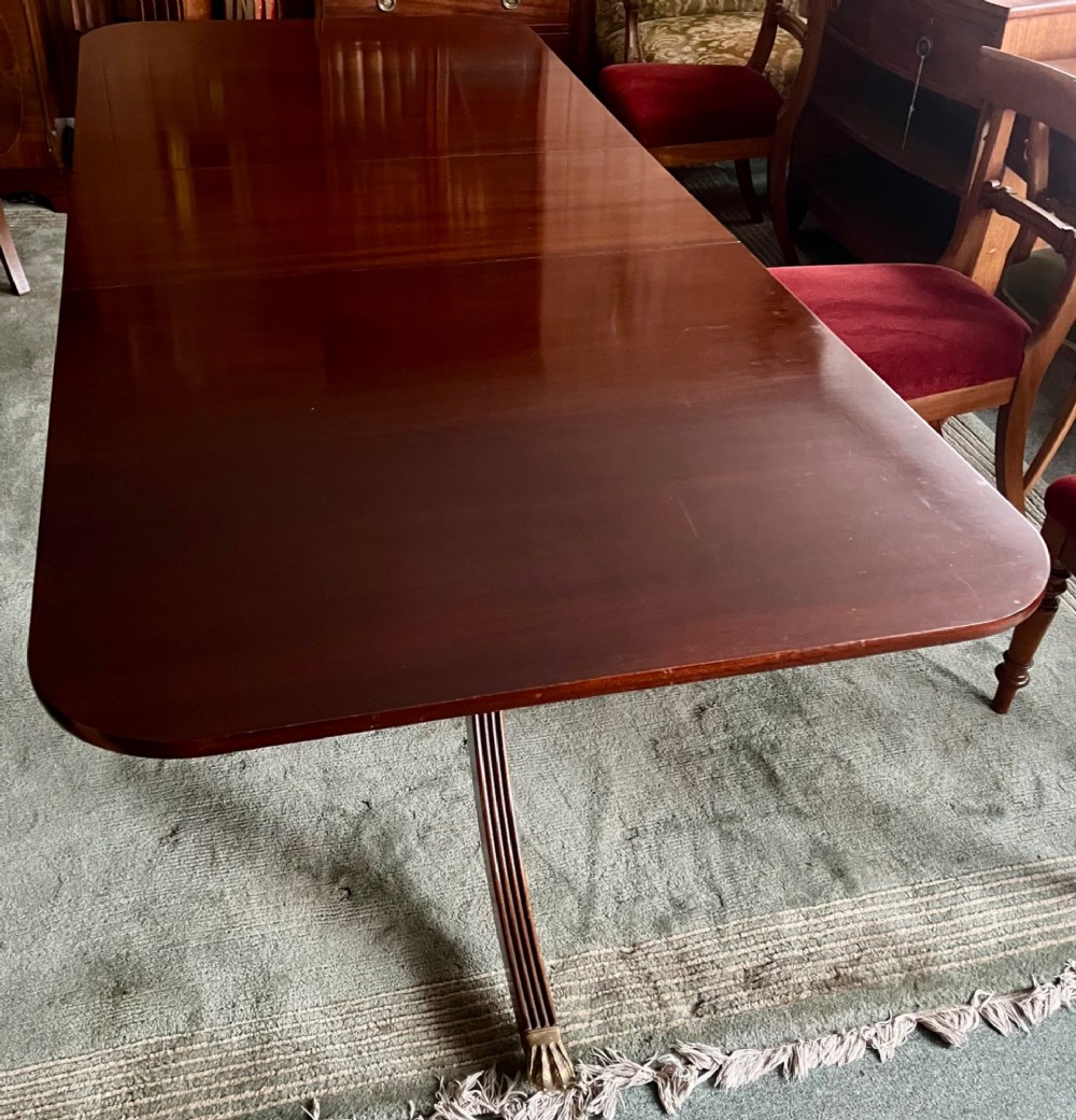 A dark brown mahogany twin pillar dining table with rounded corners and reeded splayed legs ending in brass castors.
