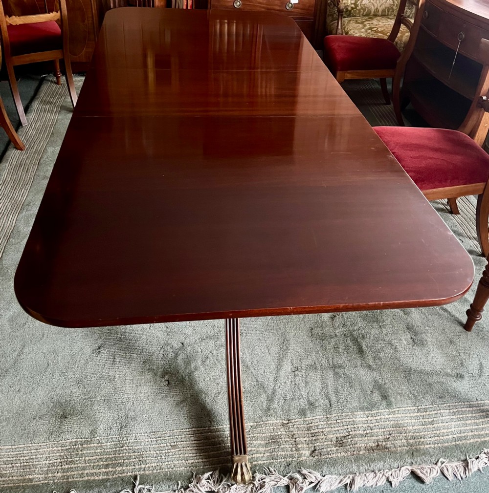 A dark brown mahogany twin pillar dining table with rounded corners and reeded splayed legs ending in brass castors. View II