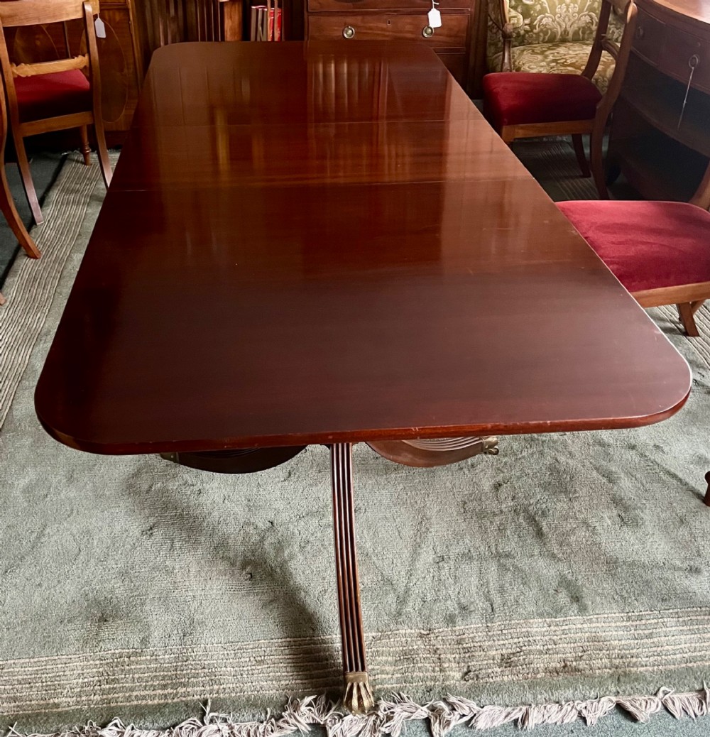 A dark brown mahogany twin pillar dining table with rounded corners and reeded splayed legs ending in brass castors. View III
