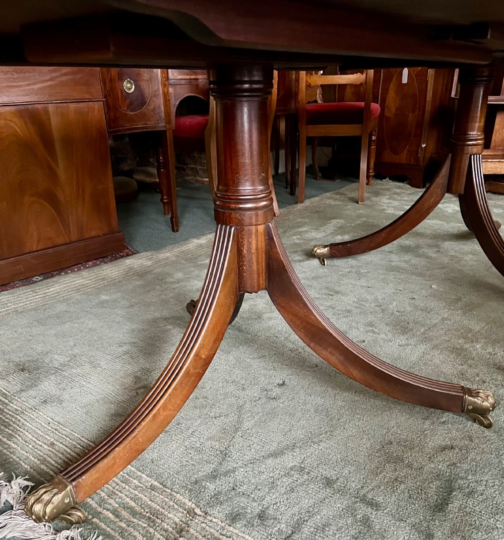A dark brown mahogany twin pillar dining table with rounded corners and reeded splayed legs ending in brass castors. View IV