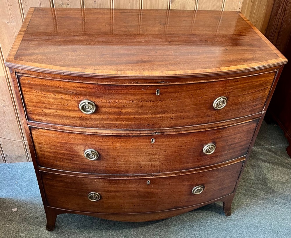 A Regency mahogany bowfront chest featuring three graduated drawers with crossbanded top inlay and brass ring handles. View II