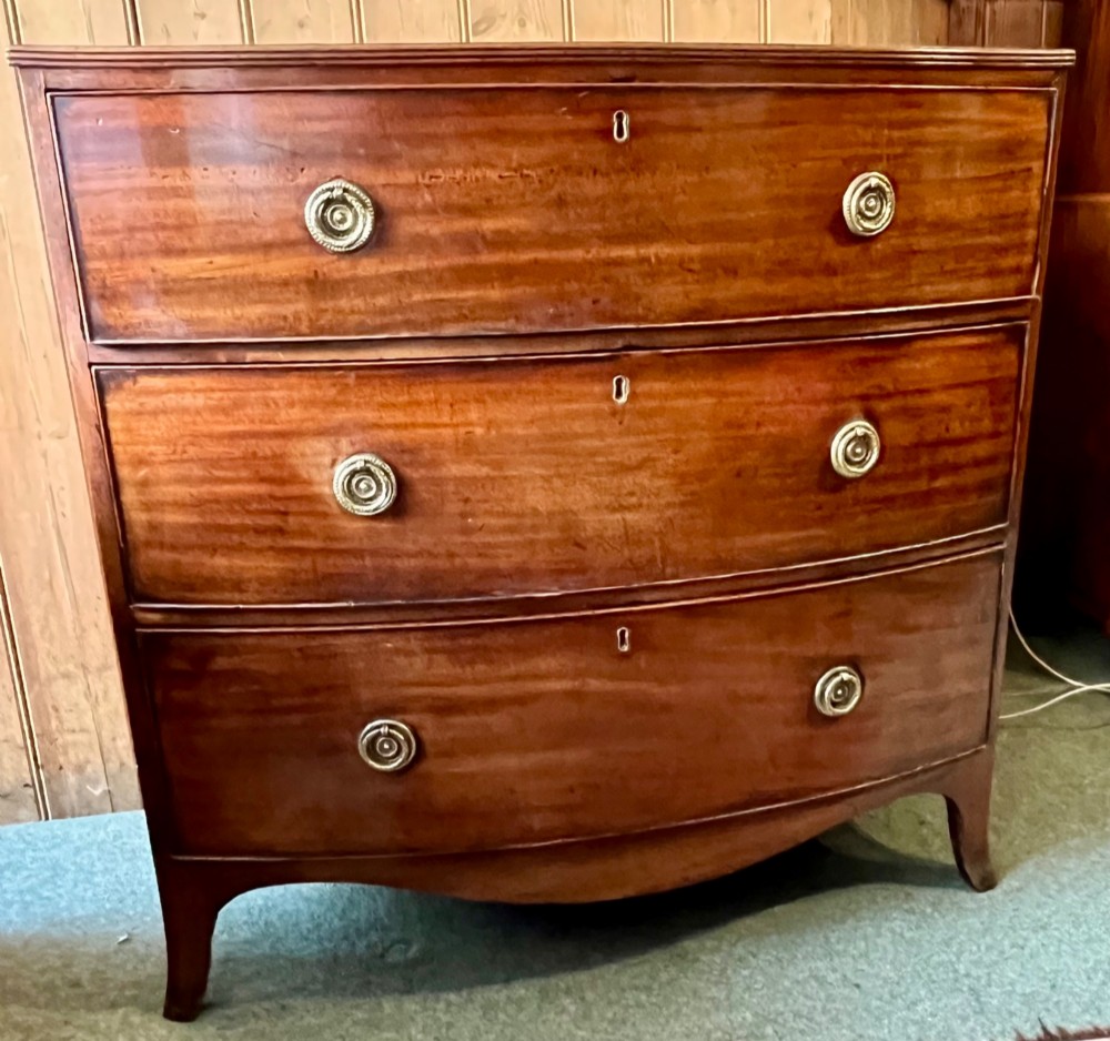 A Regency mahogany bowfront chest featuring three graduated drawers with crossbanded top inlay and brass ring handles. View III