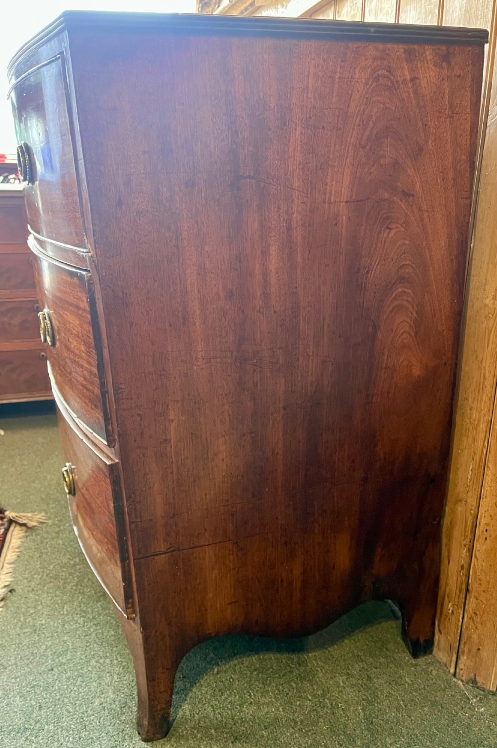 A Regency mahogany bowfront chest featuring three graduated drawers with crossbanded top inlay and brass ring handles. View IV