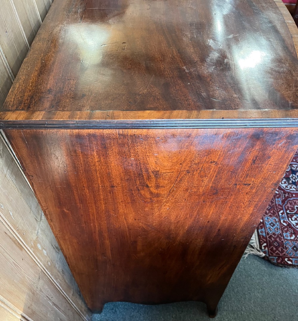A Regency mahogany bowfront chest featuring three graduated drawers with crossbanded top inlay and brass ring handles. View V