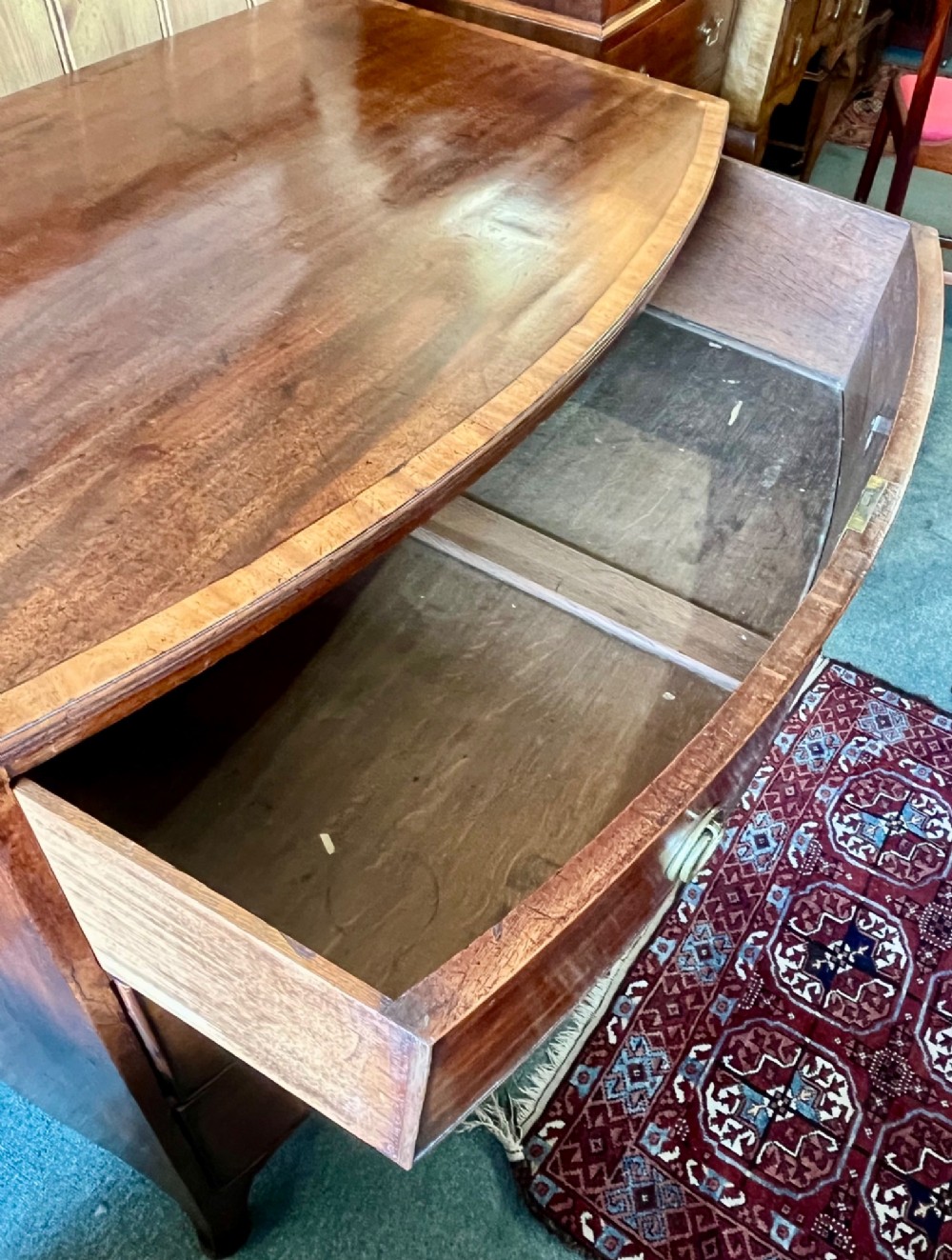 A Regency mahogany bowfront chest featuring three graduated drawers with crossbanded top inlay and brass ring handles. View VI