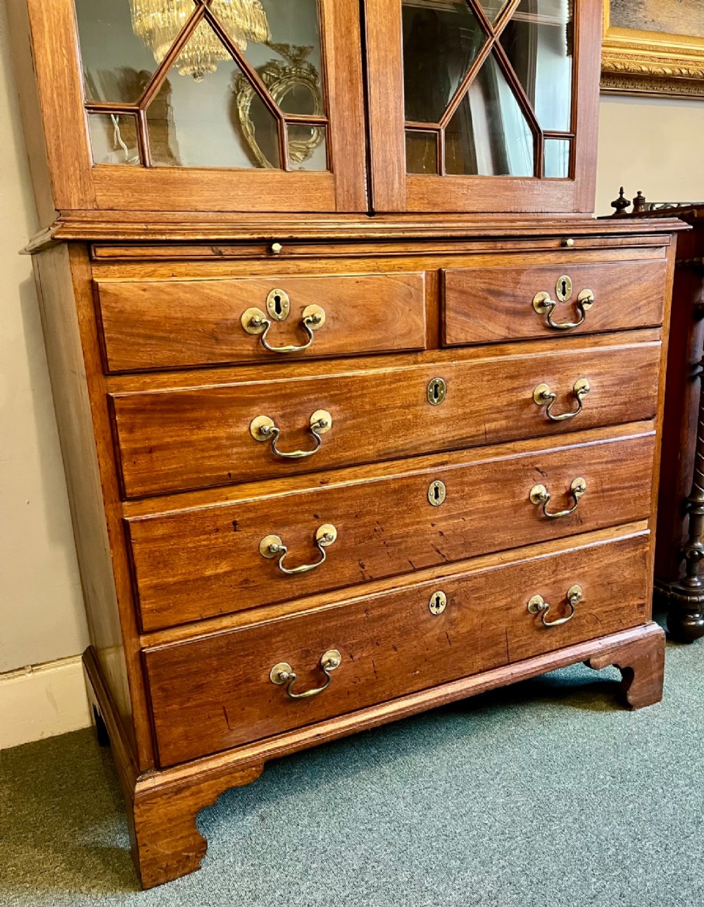 A George III mahogany library bookcase featuring astragal glazed upper doors above a chest of four drawers with brass swan-neck handles. View IV