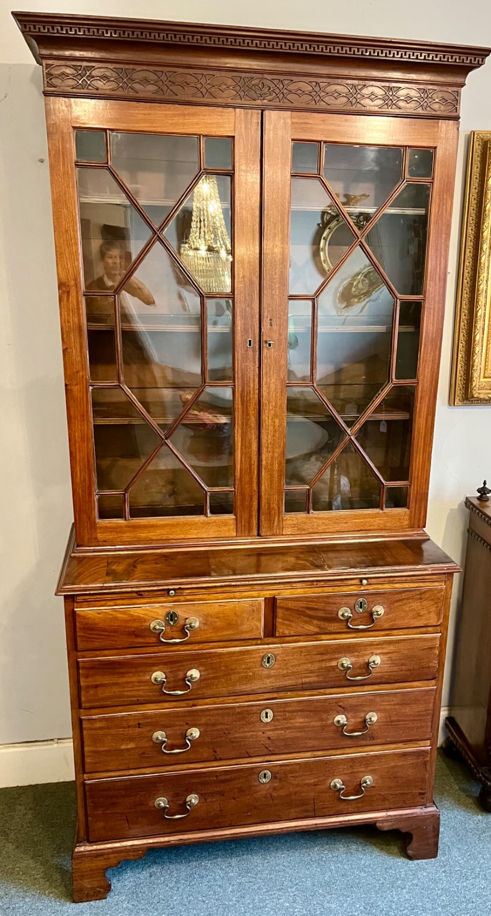 A George III mahogany library bookcase featuring astragal glazed upper doors above a chest of four drawers with brass swan-neck handles. View V