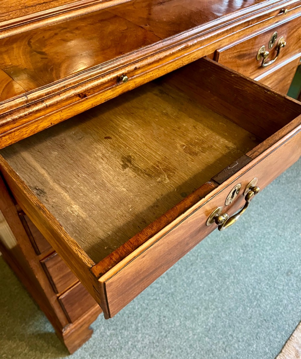 A George III mahogany library bookcase featuring astragal glazed upper doors above a chest of four drawers with brass swan-neck handles. View IX