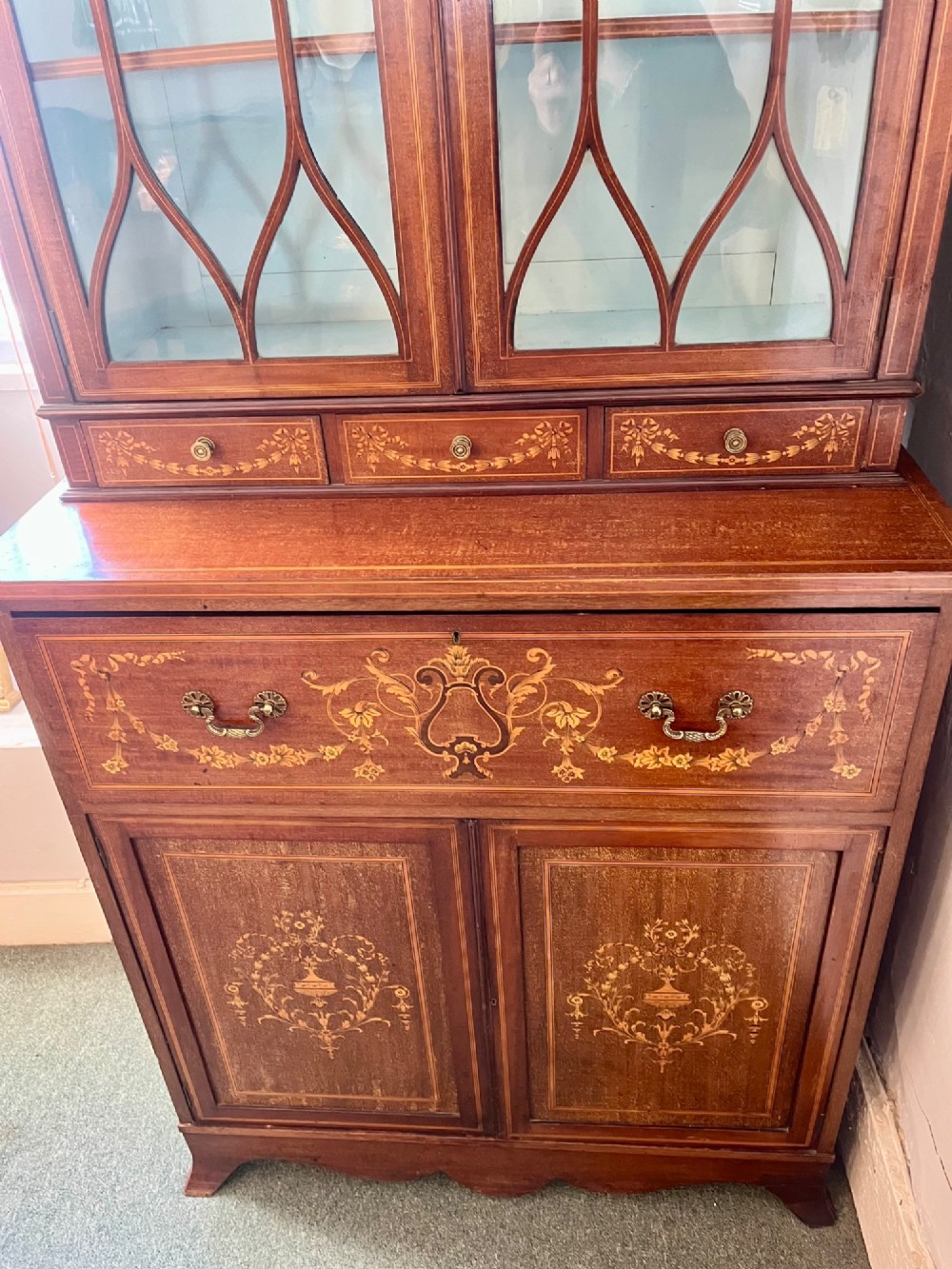 An Edwardian mahogany secretaire bookcase featuring satinwood marquetry inlays, a swan-neck pediment, glazed upper doors, and a pull-out desk drawer above lower cupboards. View IV