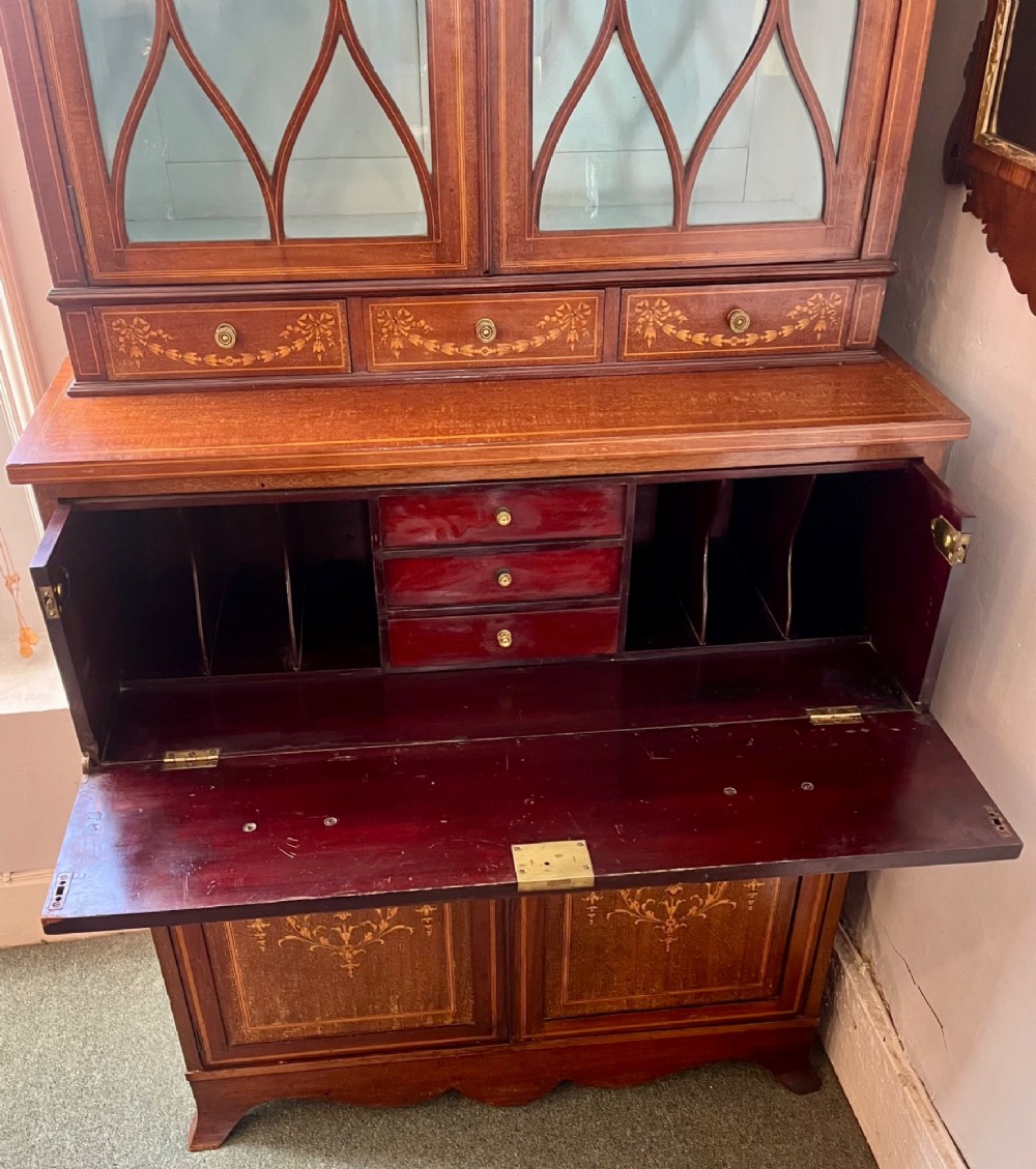 An Edwardian mahogany secretaire bookcase featuring satinwood marquetry inlays, a swan-neck pediment, glazed upper doors, and a pull-out desk drawer above lower cupboards. View IX