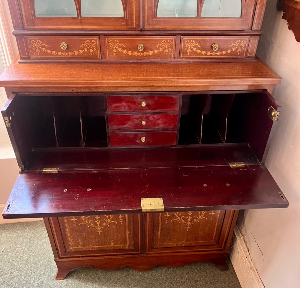 An Edwardian mahogany secretaire bookcase featuring satinwood marquetry inlays, a swan-neck pediment, glazed upper doors, and a pull-out desk drawer above lower cupboards. View X