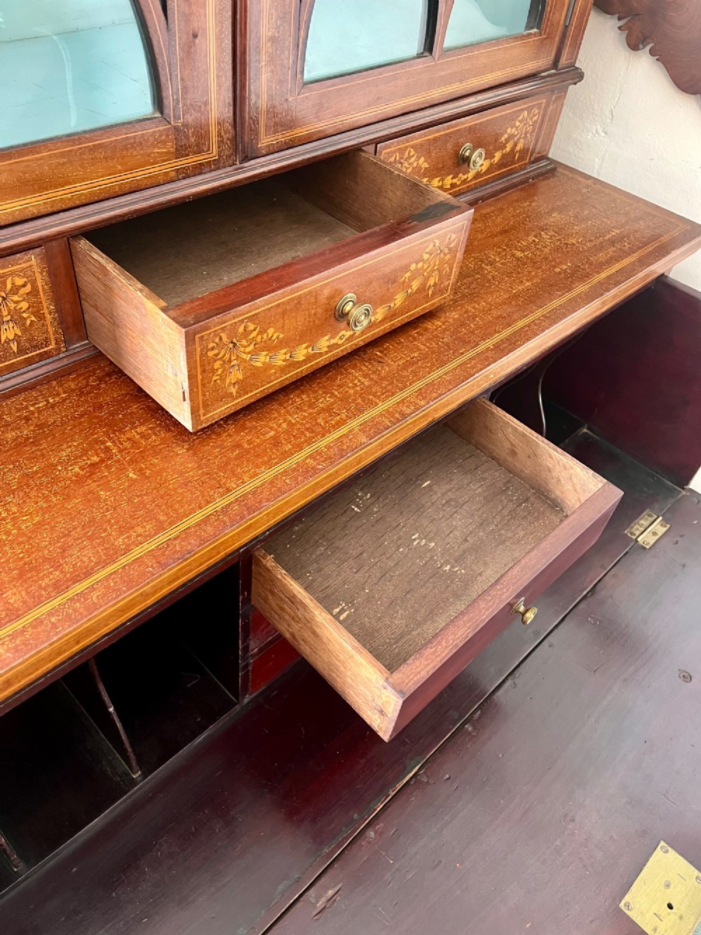 An Edwardian mahogany secretaire bookcase featuring satinwood marquetry inlays, a swan-neck pediment, glazed upper doors, and a pull-out desk drawer above lower cupboards. View XII