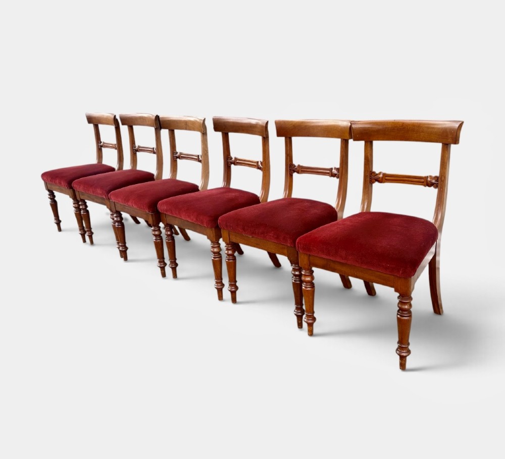 A set of six early Victorian mahogany dining chairs lined up, featuring turned front legs, curved top rails, and red velvet upholstered seats. View II