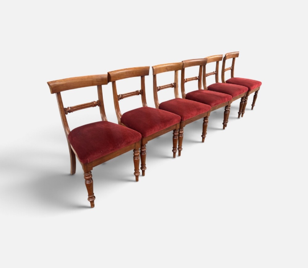 A set of six early Victorian mahogany dining chairs lined up, featuring turned front legs, curved top rails, and red velvet upholstered seats. View III