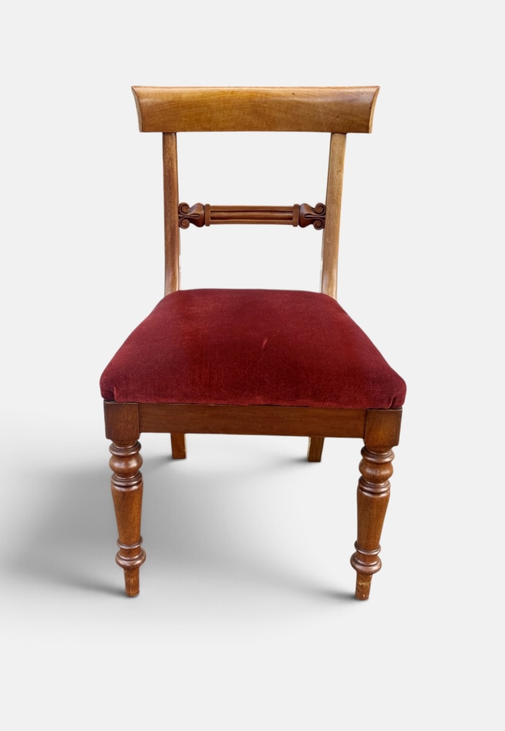A set of six early Victorian mahogany dining chairs lined up, featuring turned front legs, curved top rails, and red velvet upholstered seats. View V