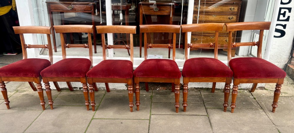 A set of six early Victorian mahogany dining chairs lined up, featuring turned front legs, curved top rails, and red velvet upholstered seats. View IX