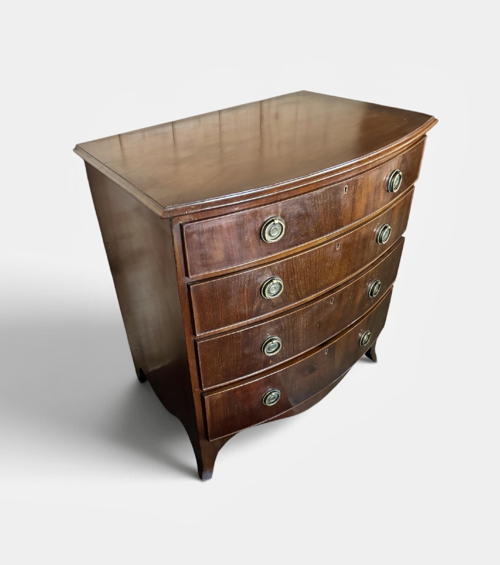 A small Edwardian mahogany bow front chest of drawers featuring four graduated drawers with brass ring drop handles and bracket feet. View IV