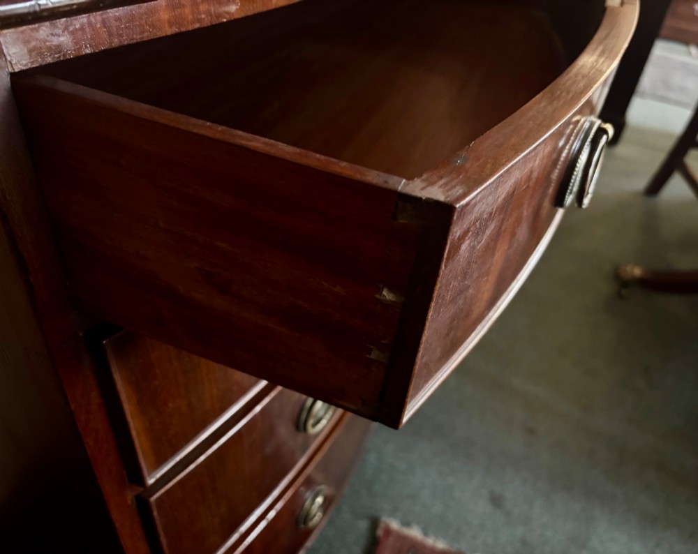 A small Edwardian mahogany bow front chest of drawers featuring four graduated drawers with brass ring drop handles and bracket feet. View V