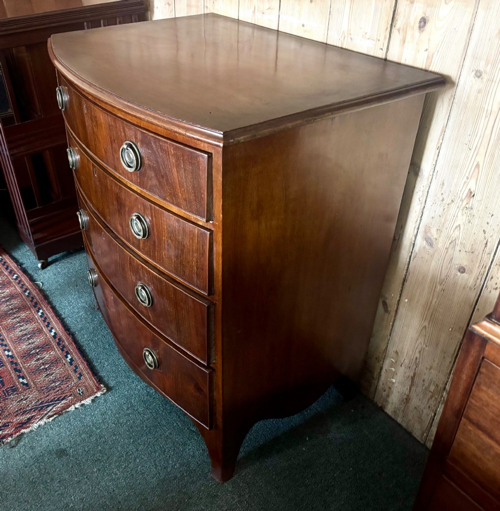A small Edwardian mahogany bow front chest of drawers featuring four graduated drawers with brass ring drop handles and bracket feet. View VI