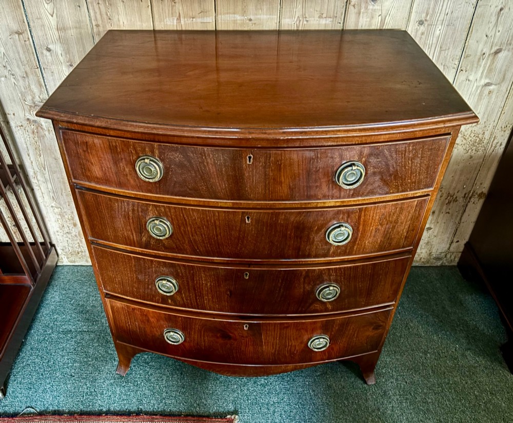 A small Edwardian mahogany bow front chest of drawers featuring four graduated drawers with brass ring drop handles and bracket feet. View VIII