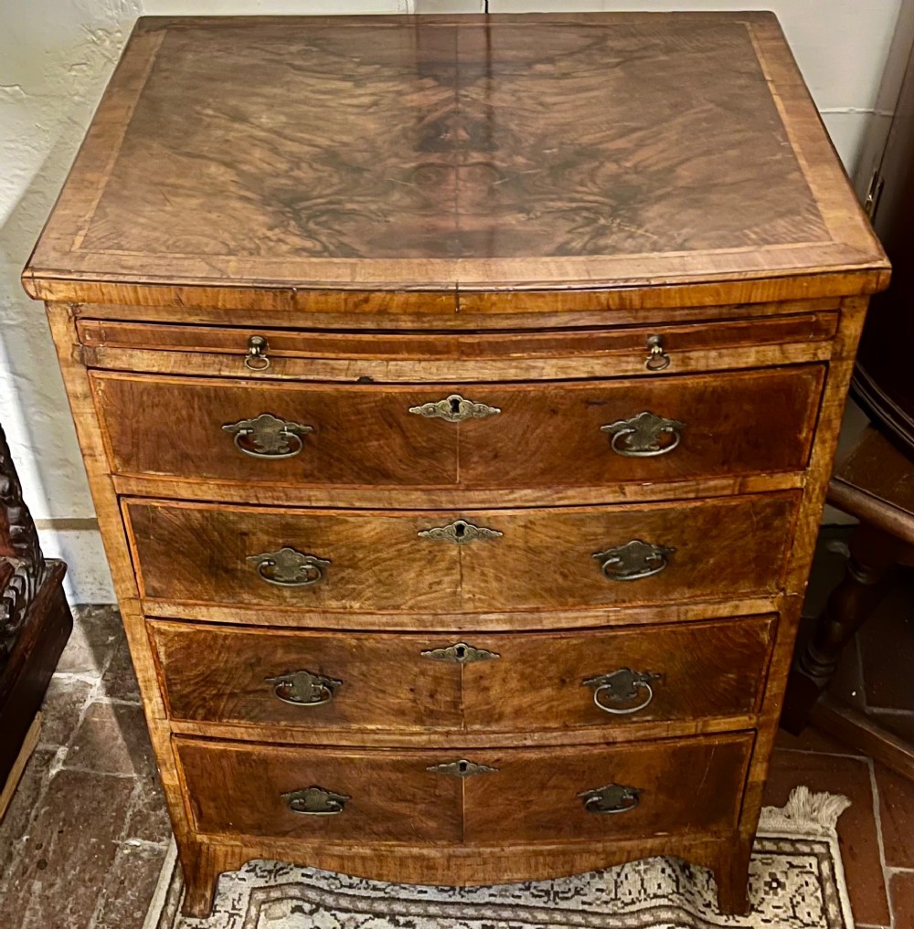 An Edwardian bow-fronted chest of drawers crafted from figured walnut with brass handles and cross-banded detailing.