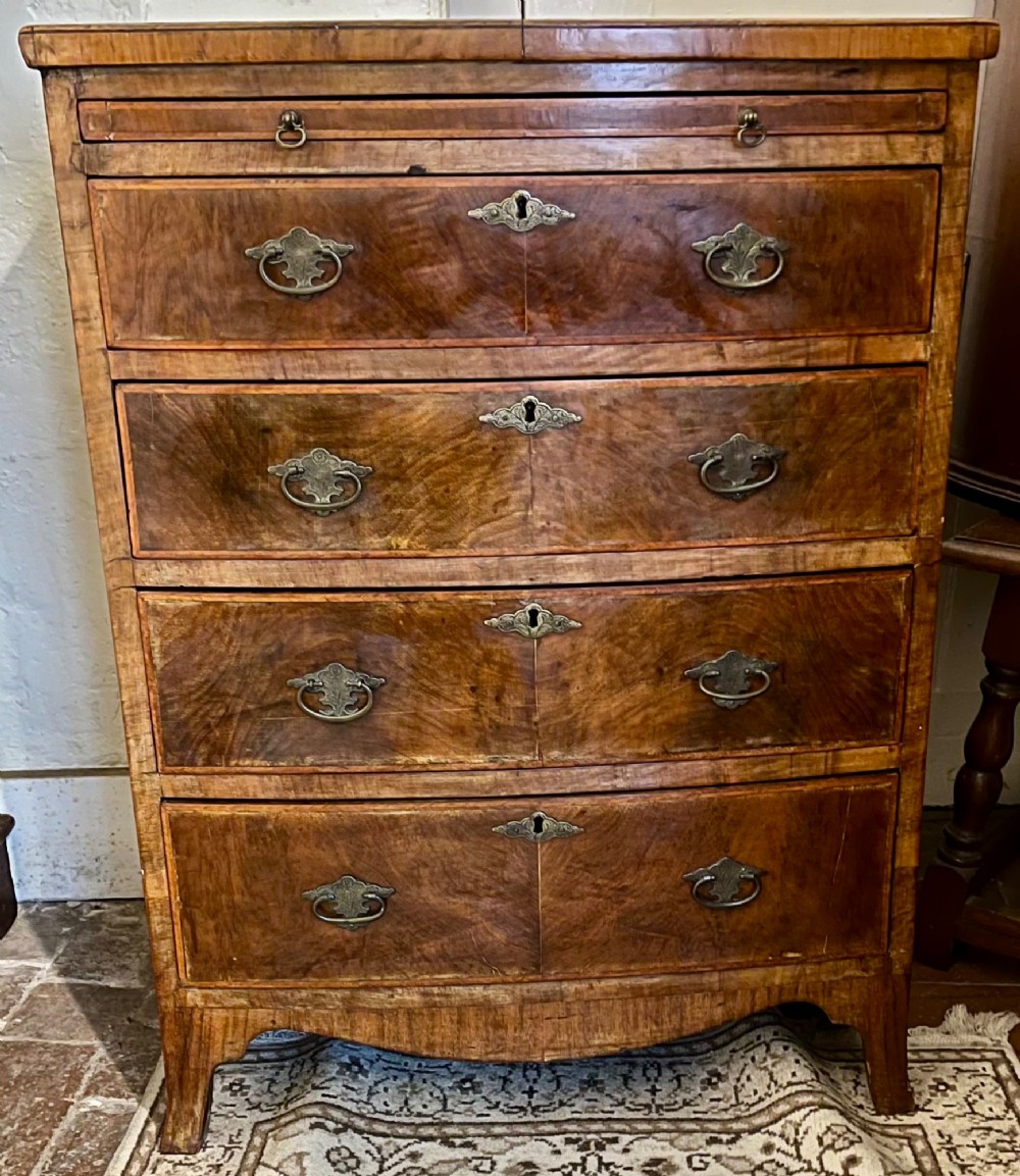 An Edwardian bow-fronted chest of drawers crafted from figured walnut with brass handles and cross-banded detailing. View IV