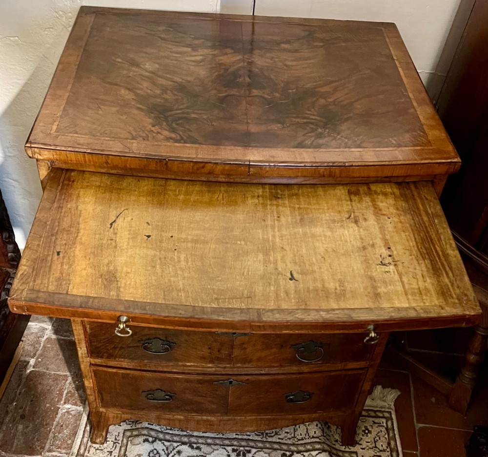 An Edwardian bow-fronted chest of drawers crafted from figured walnut with brass handles and cross-banded detailing. View V