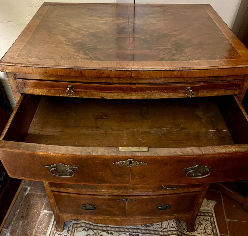 An Edwardian bow-fronted chest of drawers crafted from figured walnut with brass handles and cross-banded detailing. View VI