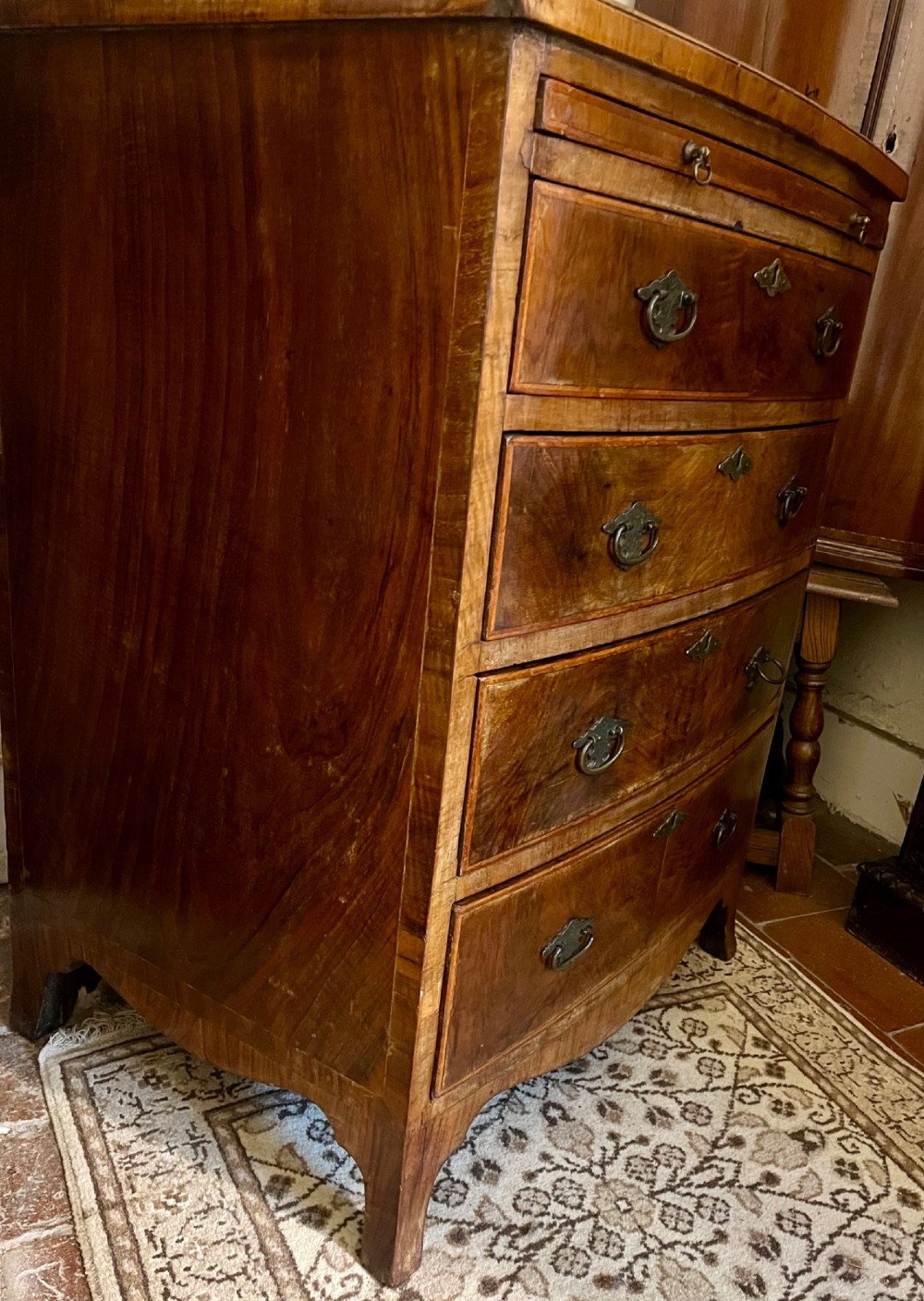 An Edwardian bow-fronted chest of drawers crafted from figured walnut with brass handles and cross-banded detailing. View VII