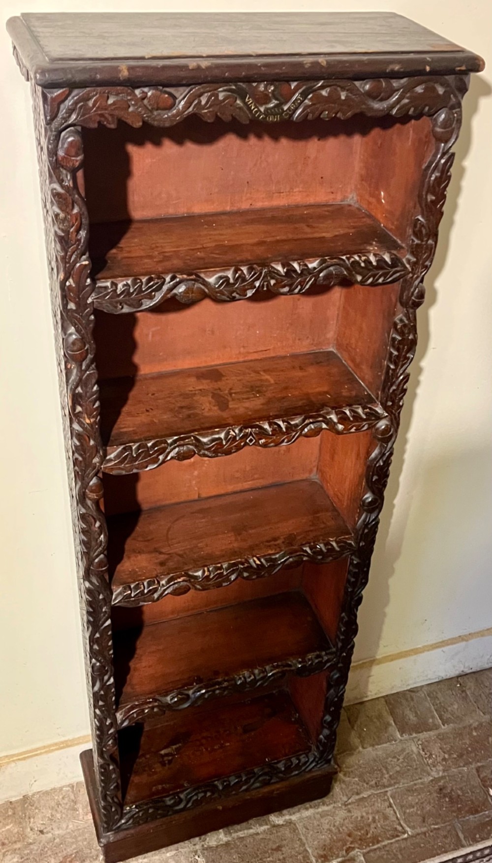 A tall, narrow Victorian open bookcase made of dark carved oak and pine with five shelves decorated with leaf borders.