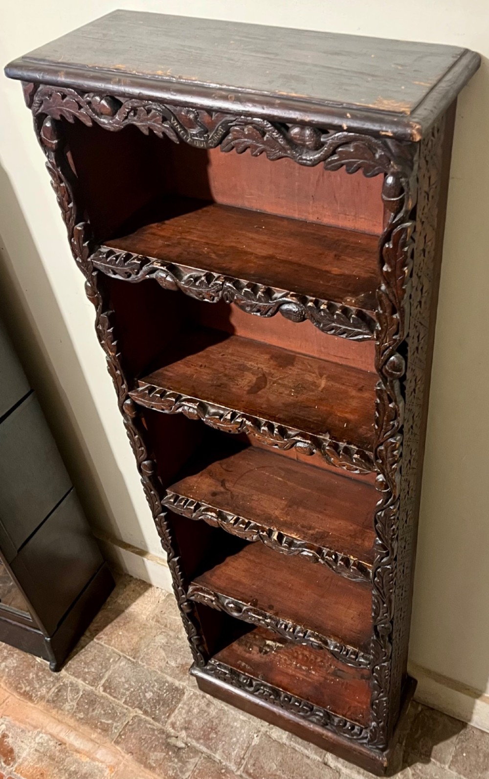 A tall, narrow Victorian open bookcase made of dark carved oak and pine with five shelves decorated with leaf borders. View V