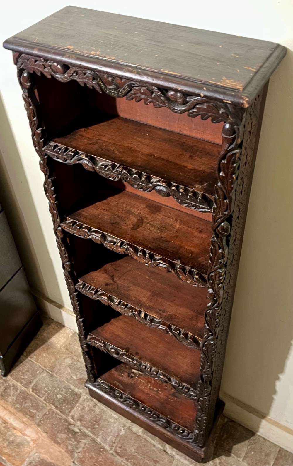 A tall, narrow Victorian open bookcase made of dark carved oak and pine with five shelves decorated with leaf borders. View VI
