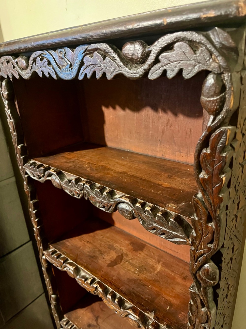 A tall, narrow Victorian open bookcase made of dark carved oak and pine with five shelves decorated with leaf borders. View X