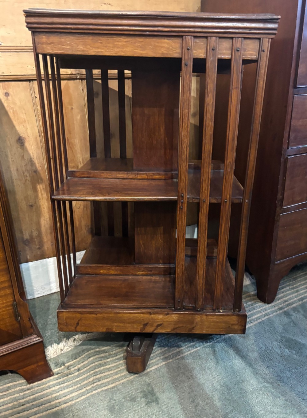 An Edwardian oak revolving bookcase featuring two tiers with vertical slatted sides mounted on a rotating central base. View II