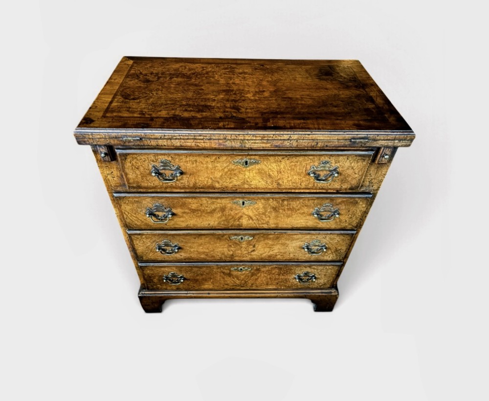 An antique burr walnut bachelors chest featuring a hinged fold-over top, four graduated drawers with brass handles, and bracket feet.