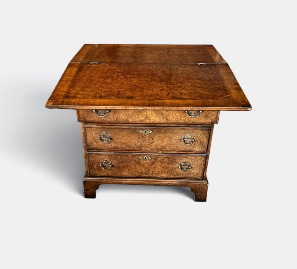 An antique burr walnut bachelors chest featuring a hinged fold-over top, four graduated drawers with brass handles, and bracket feet. View II