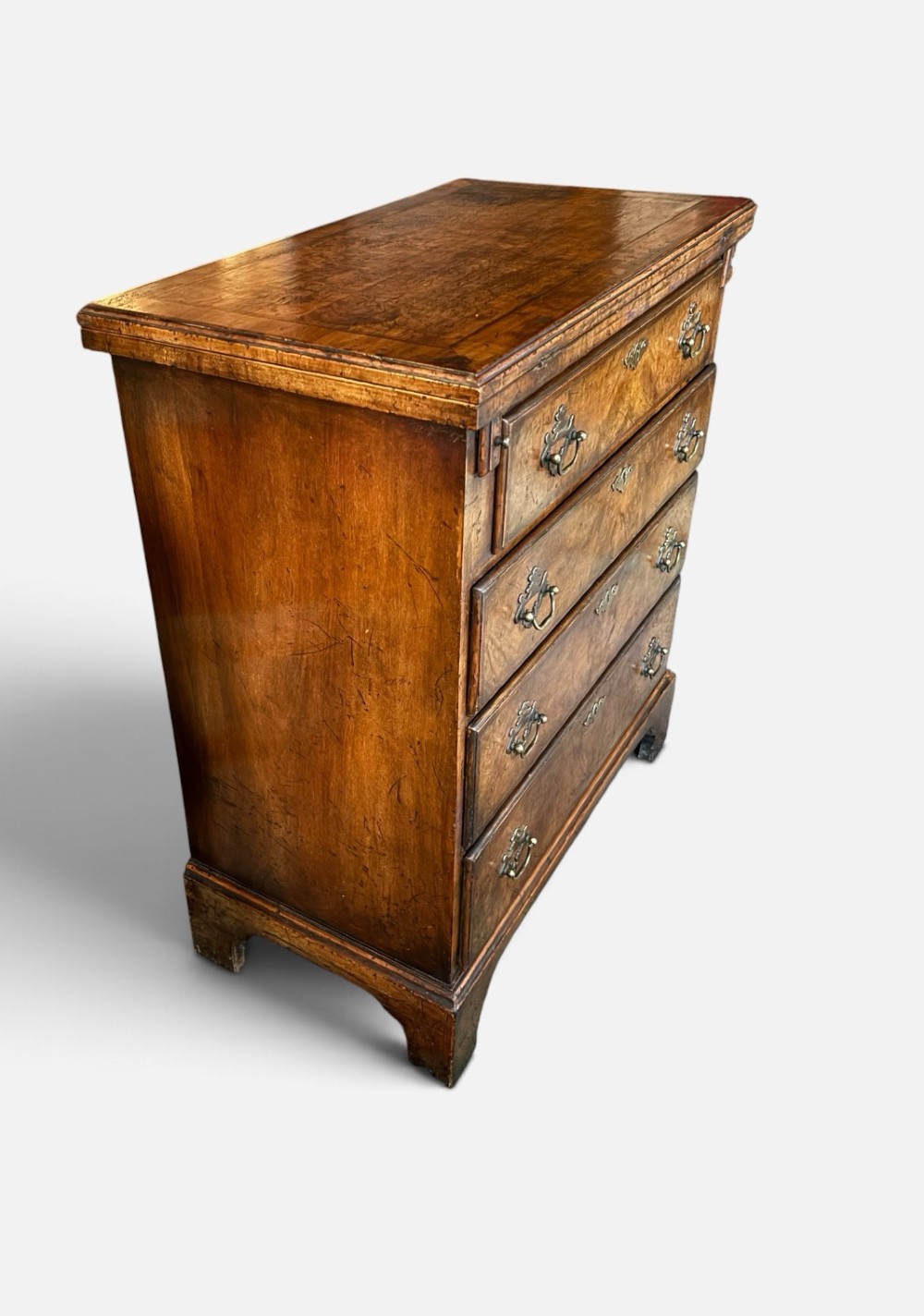 An antique burr walnut bachelors chest featuring a hinged fold-over top, four graduated drawers with brass handles, and bracket feet. View V