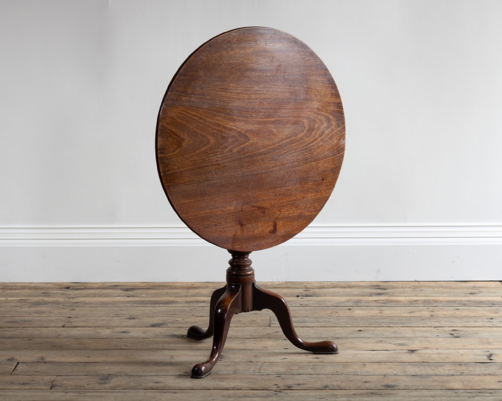 A George III mahogany tripod table displayed with its circular top tilted vertically on a central turned column and three cabriole legs.