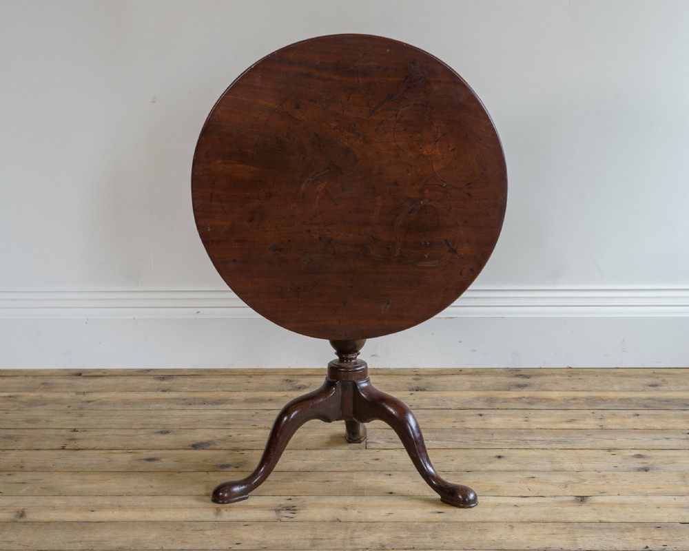 A George II mahogany tripod table featuring a circular tilt-top surface mounted on a turned pedestal stem and three cabriole legs with pad feet.