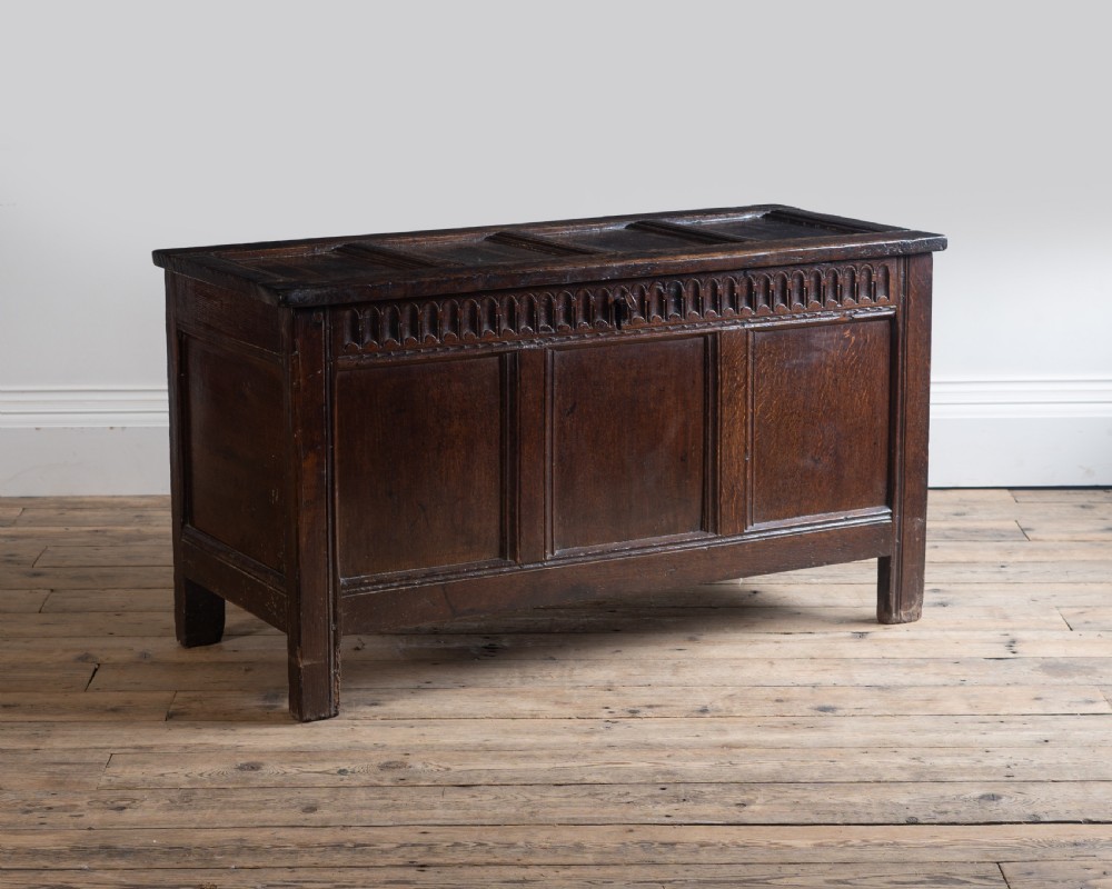 A late 17th century dark oak coffer featuring a carved upper frieze, three panelled front sections, and a hinged panelled lid.
