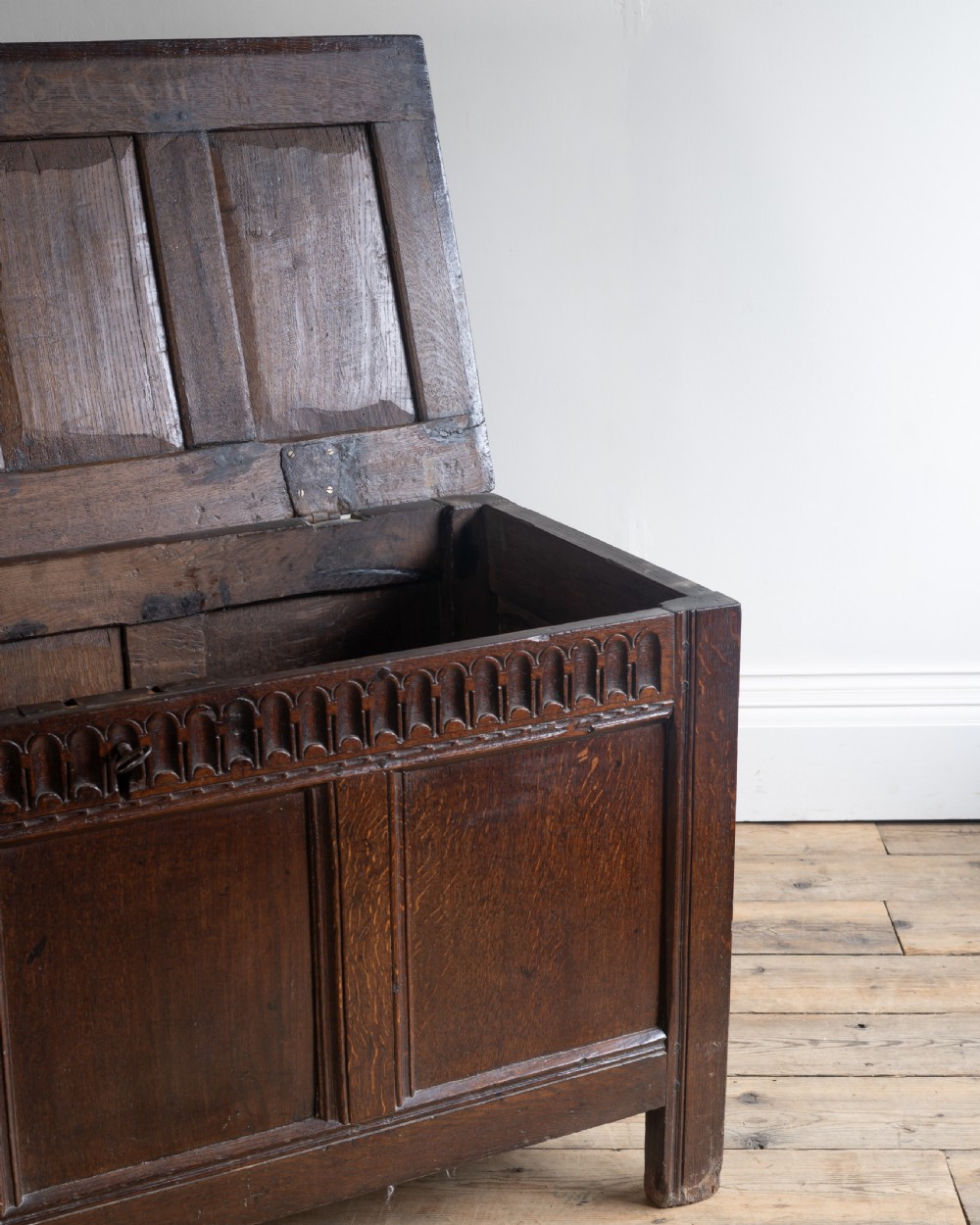 A late 17th century dark oak coffer featuring a carved upper frieze, three panelled front sections, and a hinged panelled lid. View II