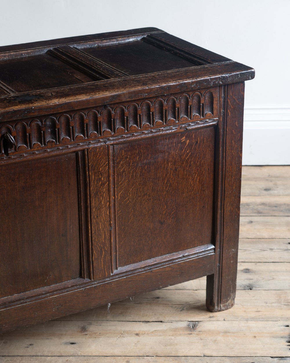 A late 17th century dark oak coffer featuring a carved upper frieze, three panelled front sections, and a hinged panelled lid. View III