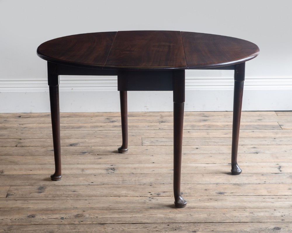 A Georgian dark mahogany oval supper table featuring two drop leaves supported by slender legs with pad feet.