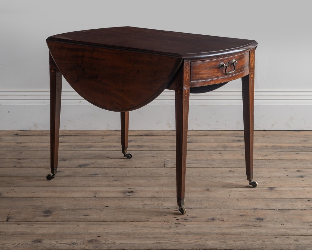 A George III mahogany Pembroke table with rounded drop leaves, a single drawer with brass pull handle, and tapered legs ending in brass castors.