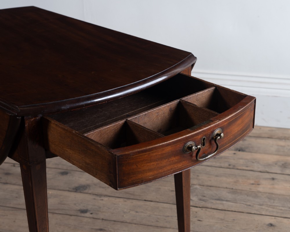 A George III mahogany Pembroke table with rounded drop leaves, a single drawer with brass pull handle, and tapered legs ending in brass castors. View II