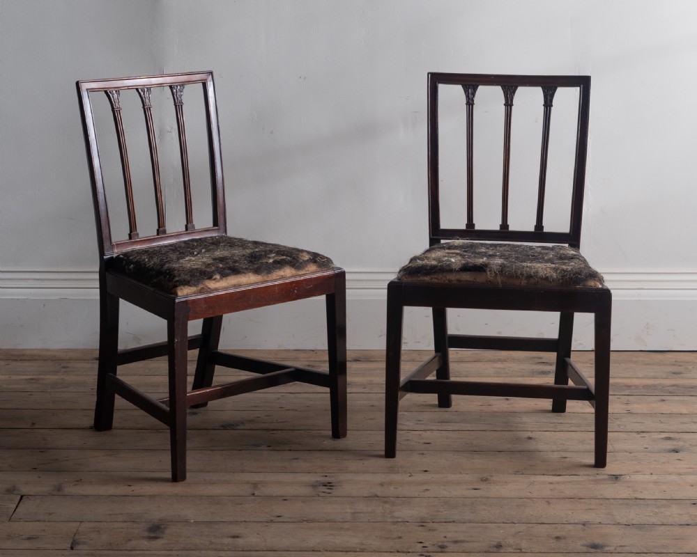 A pair of dark mahogany George III side chairs featuring rectangular backs with vertical reeded splats, square legs, and upholstered drop-in seats.