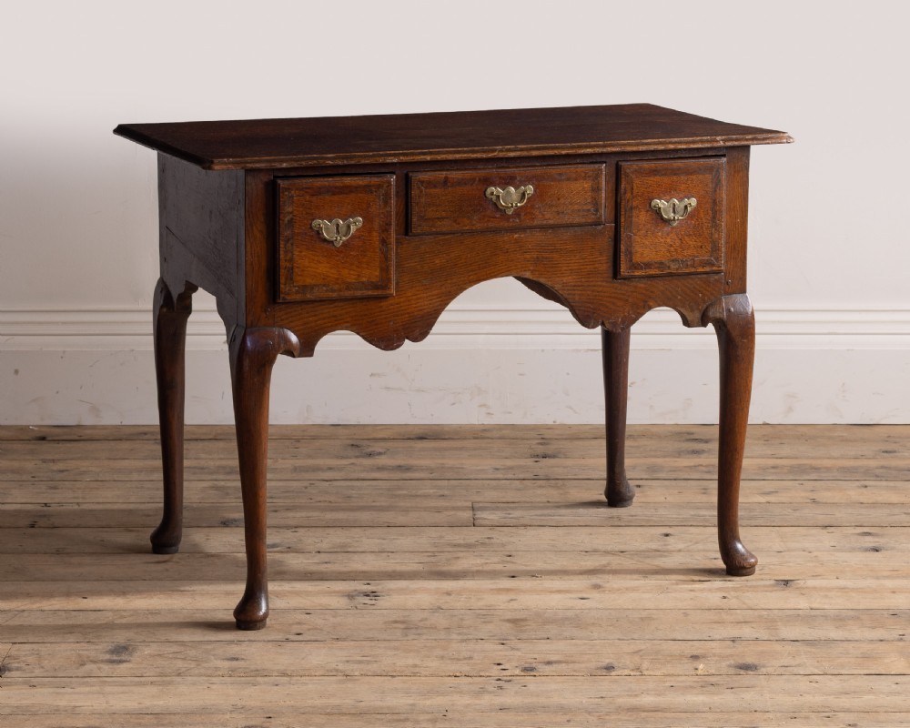A Georgian oak low boy featuring three drawers with brass handles, a shaped apron, and cabriole legs resting on pad feet.