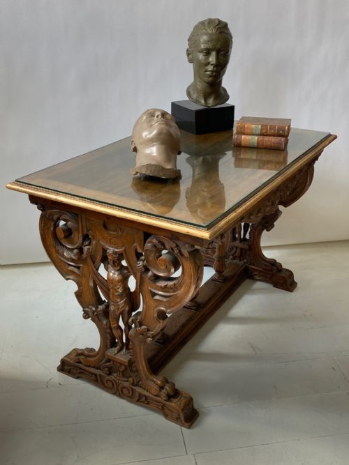 fig 1. A 19th-century carved walnut library table featuring intricate trestle end supports with carved figurative male terms and scrolled foliage.