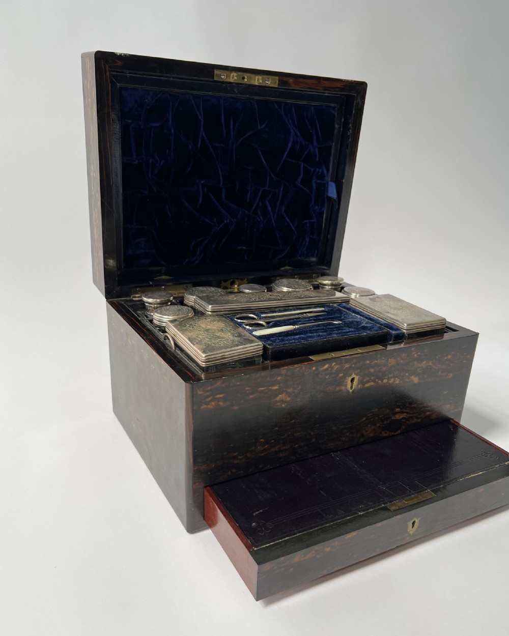A nineteenth-century dark coromandel wood dressing case open to reveal dark blue velvet interior lining, fitted silver-topped glass bottles, vanity implements, and an extended lower drawer.