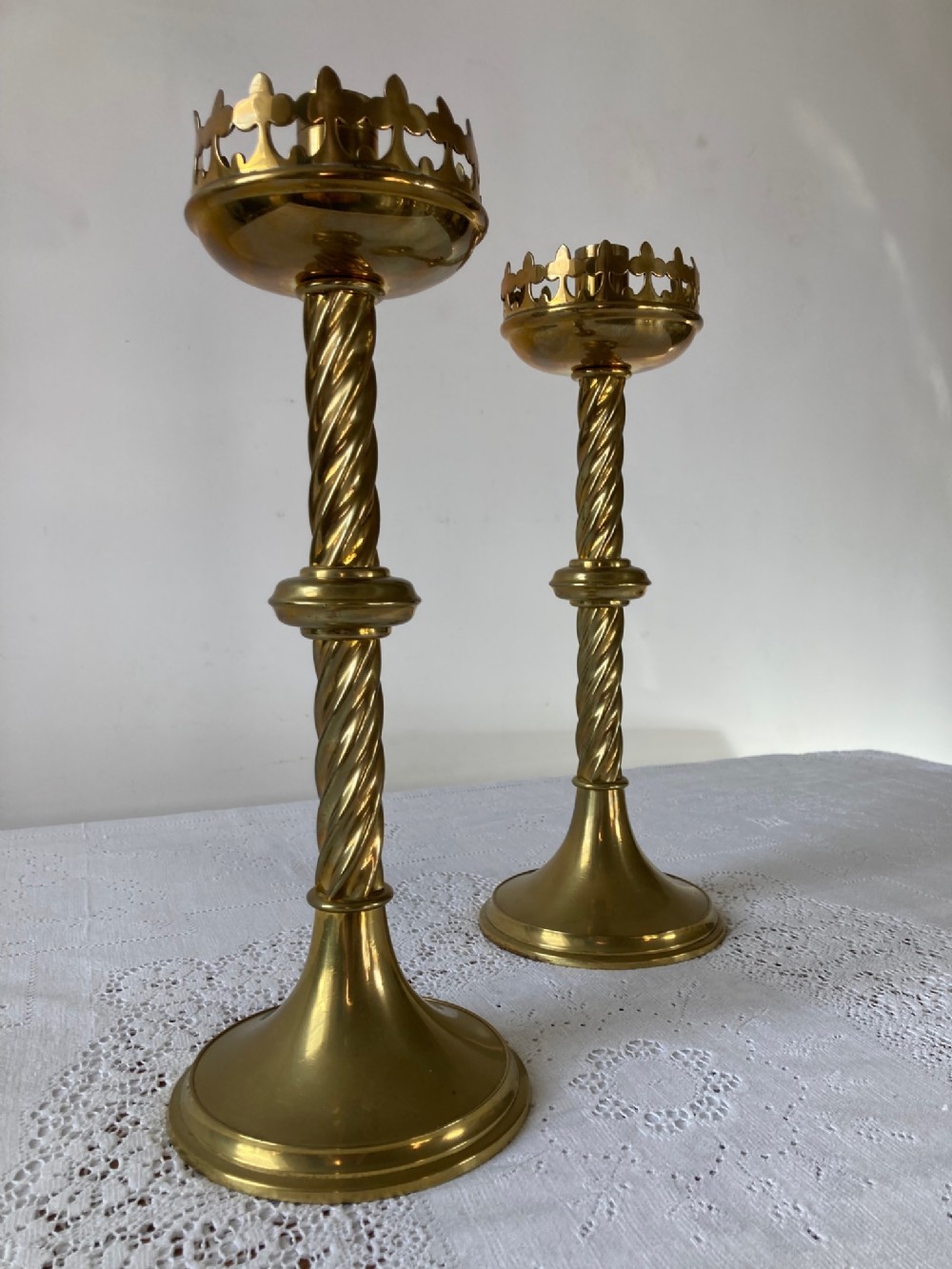 A pair of polished brass Gothic Revival candlesticks featuring spiral twist stems, crenellated top sconces, and circular flared bases.